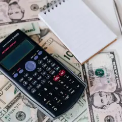 Kalkulator, notatnik i banknoty dolarów. Obliczanie, ile kosztuje metr sześcienny gazu, wymaga dokładnych danych.