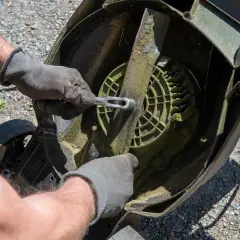 Ręce w rękawiczkach odkręcają nóż kosiarki.