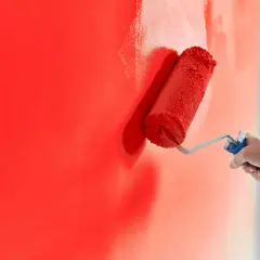 Malowanie ściany na intensywny czerwony kolor. Zastanawiasz się, ile schnie farba na ścianie? Proces malowania jest w toku.
