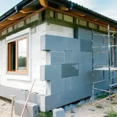 Budowa domu, ocieplenie ścian zewnętrznych szarymi bloczkami, rusztowanie.