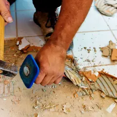 Skuwanie płytek cena: pracownik młotkiem i dłutem usuwa stare płytki z podłogi, przygotowując ją do remontu.
