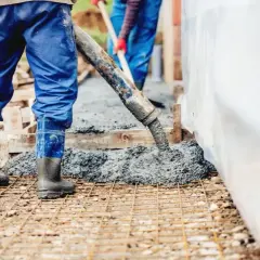 Pracownicy wylewają beton na zbrojenie. Sprawdź aktualną suchy beton cena 1m3.