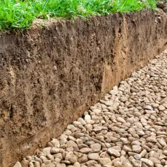 Wykop pod fundamenty, odsłaniający warstwy gleby i kamieni. Widać zieloną trawę na górze, a poniżej ziemię z korzeniami. To ważna strefa przemarzania.