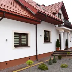 Elegancki cokół na elewacji domu, podkreślony brązowymi rynnami i ozdobnymi schodami.