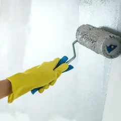 Ręka w żółtej rękawicy maluje ścianę wałkiem do farby lateksowej.