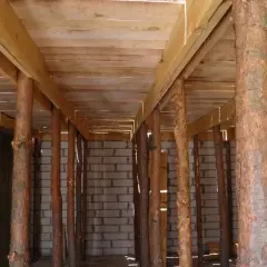 Szalowanie stropu z drewnianych belek i pni drzew, podtrzymujące konstrukcję nad ścianami z bloczków.