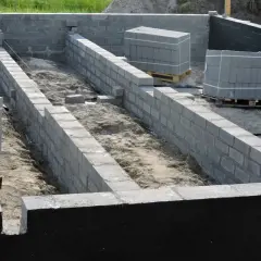 Budowa fundamentów z bloczków betonowych, przygotowanie pod ocieplanie fundamentów. Materiały budowlane czekają na użycie.