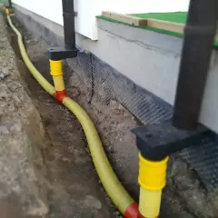 System odprowadzenia wody z rynien w żółtej rurze, biegnącej w wykopie przy fundamencie domu.