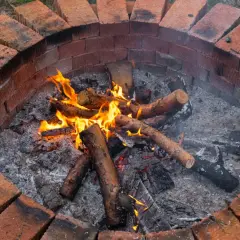 Ognisko w ogrodzie z cegły, płonące drewno w popiele.