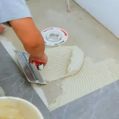 Płytkarz rozprowadza klej kielnią zębatą, przygotowując podłoże pod płytki 60x60.