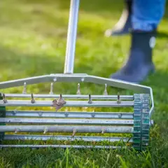 Wertykulator na trawniku, przygotowujący go do rekultywacji. Widać kolce i fragmenty butów osoby pracującej.