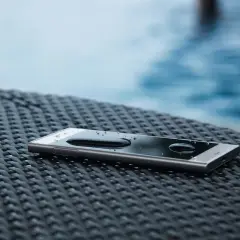 Telefon z kroplami wody na ekranie, leżący na plecionej powierzchni. IP65 co oznacza? Ochrona przed pyłem i strumieniem wody.