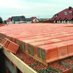 Strop ackermana w budowie, rzędy pustaków ceramicznych czekają na betonowanie. W tle domy z czerwonymi dachami.