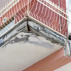 Zniszczony balkon z widocznymi ubytkami w betonie i zardzewiałym zbrojeniem. Idealne miejsce, by zastanowić się, czym uzupełnić ubytki w betonie na zewnątrz.