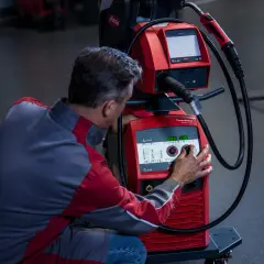 Mężczyzna w kombinezonie ustawia parametry na spawarce inwertorowej Fronius.