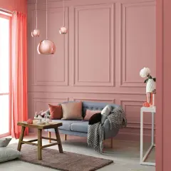 Przytulny salon w odcieniach różu i koralu. Na ścianach subtelny wzór, a w centralnym punkcie wygodna kanapa. Kolor waniliowy subtelnie podkreśla elegancję wnętrza.