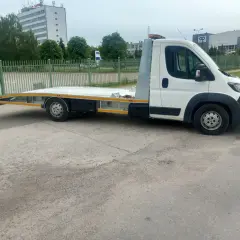 Biała laweta z platformą stoi na parkingu. Zastanawiasz się, ile kosztuje laweta?