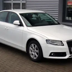 Białe Audi A4 B8 sedan zaparkowane na bruku przed budynkiem.