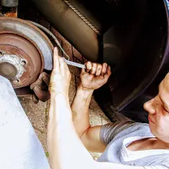 Młody mechanik z brudnymi rękami przykręca śrubę przy kole. Zastanawia się nad wymiana łożyska w kole cena.