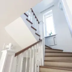 Jasne schody z drewnianymi stopniami i białymi balustradami. Inspiracja, jak tanio wykończyć schody betonowe, by wyglądały elegancko.