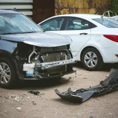Uszkodzony szary samochód i biały sedan na placu złomowiska. Zastanawiasz się, ile kosztuje złomowanie auta?