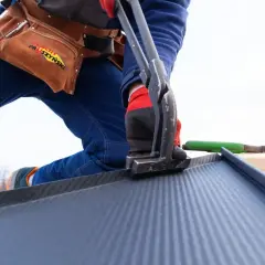 Dekarz pracuje nad dachem, używając narzędzi do blachy. Poznaj cenę robocizny dachu za m2.