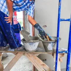Pracownik na rusztowaniu przygotowuje zaprawę. Tynkowanie ścian cena zależy od wielu czynników.