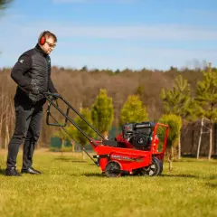 Mężczyzna w słuchawkach i okularach prowadzi czerwoną aerator. Idealny czas na aerację trawnika, by zapewnić mu zdrowy wzrost.