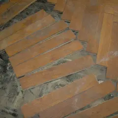 Drewniane deski parkietu, niektóre luźne, czekają na ułożenie. Subit, klej do parkietu, jest gotowy do pracy.