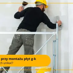 Fachowiec w żółtym kasku i roboczych spodniach pracuje na rusztowaniu, nakładając gładź na ścianę. To praca przy **suchej zabudowie**.