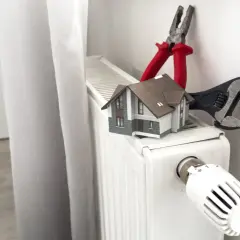 Model domu, klucz francuski i kombinerki na grzejniku.