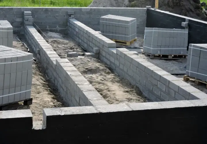 Budowa fundamentów z bloczków betonowych, przygotowanie pod ocieplanie fundamentów. Materiały budowlane czekają na użycie.