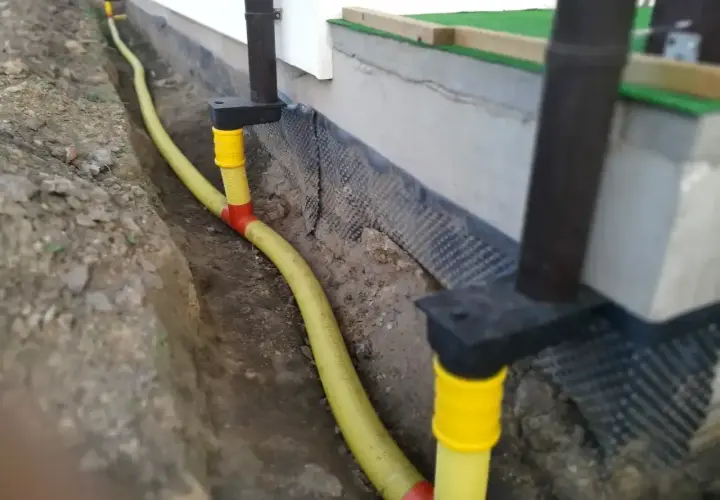 System odprowadzenia wody z rynien w żółtej rurze, biegnącej w wykopie przy fundamencie domu.