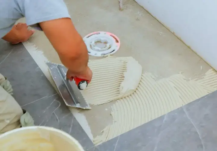 Płytkarz rozprowadza klej kielnią zębatą, przygotowując podłoże pod płytki 60x60.