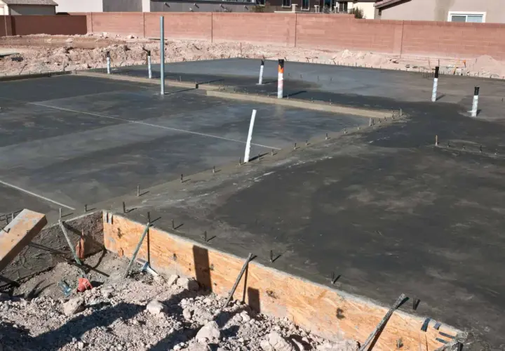 Świeżo wylany beton na płycie fundamentowej, widoczne rury i zbrojenie. Trwa izolacja pozioma fundamentów.