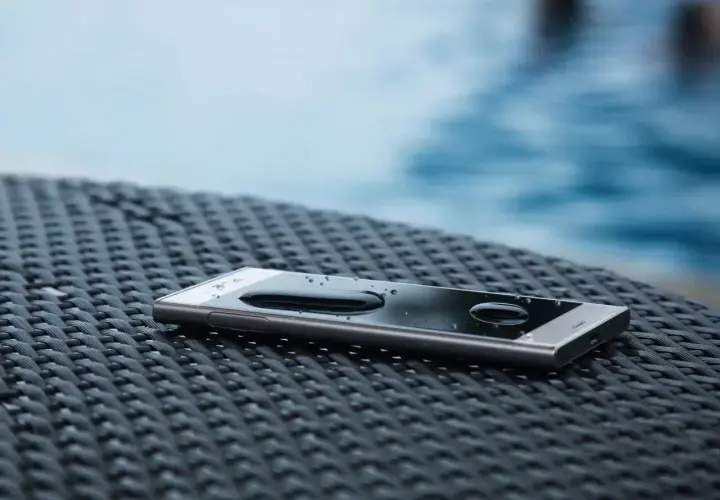 Telefon z kroplami wody na ekranie, leżący na plecionej powierzchni. IP65 co oznacza? Ochrona przed pyłem i strumieniem wody.