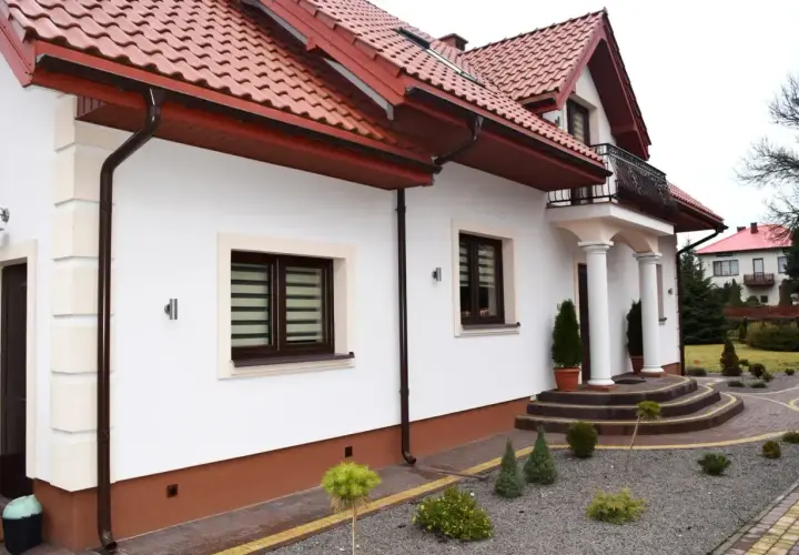 Nowy, biały tynk elewacji lśni na słońcu, podkreślając nowoczesny styl domu.