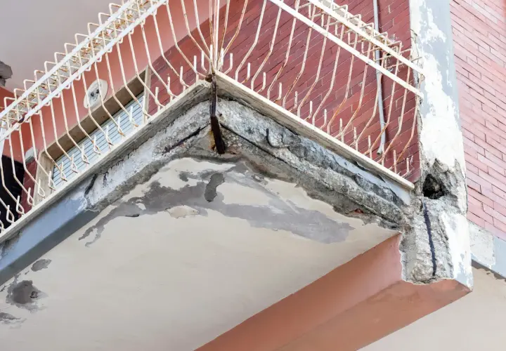 Zniszczony balkon z widocznymi ubytkami w betonie i zardzewiałym zbrojeniem. Idealne miejsce, by zastanowić się, czym uzupełnić ubytki w betonie na zewnątrz.