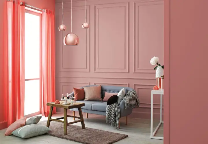 Przytulny salon w odcieniach różu i koralu. Na ścianach subtelny wzór, a w centralnym punkcie wygodna kanapa. Kolor waniliowy subtelnie podkreśla elegancję wnętrza.