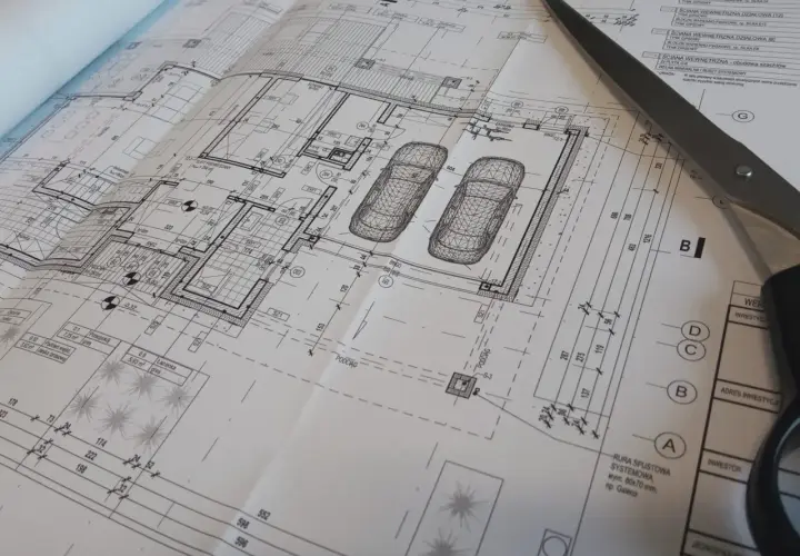 Szare nożyczki przecinają szczegółowy projekt budowlany domu z garażem.