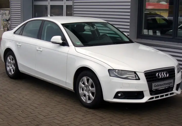 Białe Audi A4 B8 sedan zaparkowane na bruku przed budynkiem.
