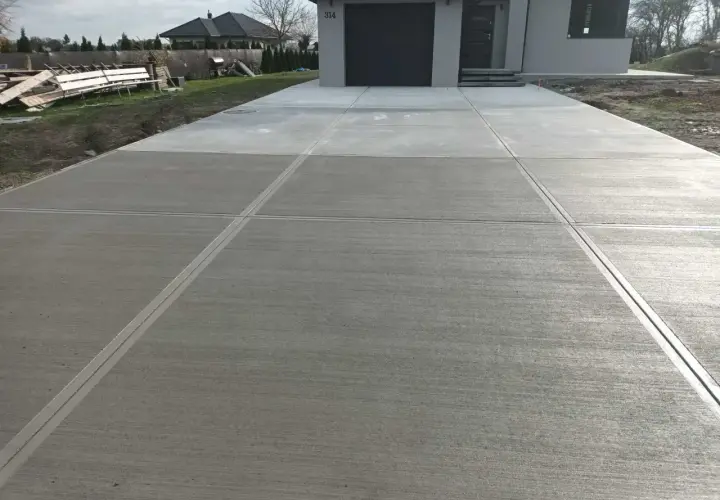 Nowy podjazd z beton stemplowany, z wyraźnymi liniami podziału, prowadzi do nowoczesnego domu.