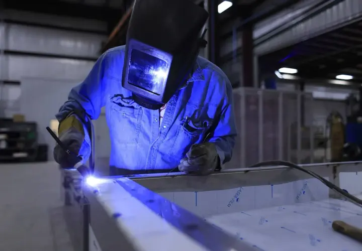 Spawanie aluminium migomatem. Pracownik w masce spawalniczej łączy metalowe elementy, tworząc jasny łuk.