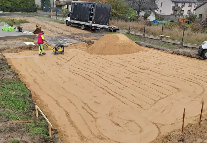 Pracownik zagęszcza piasek zagęszczarką. Trwają prace ziemne, ustalana jest korytowanie cena za m2.