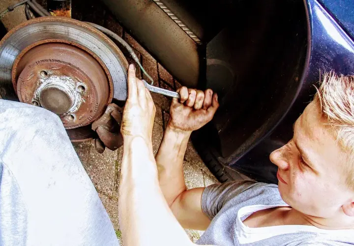 Młody mechanik z brudnymi rękami przykręca śrubę przy kole. Zastanawia się nad wymiana łożyska w kole cena.