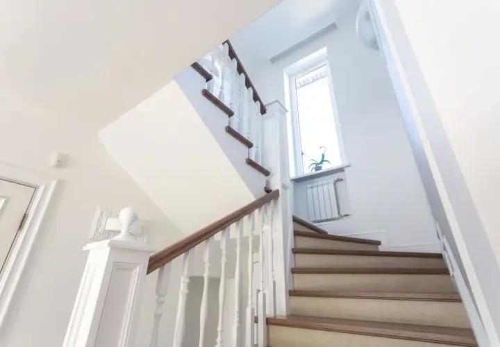 Jasne schody z drewnianymi stopniami i białymi balustradami. Inspiracja, jak tanio wykończyć schody betonowe, by wyglądały elegancko.