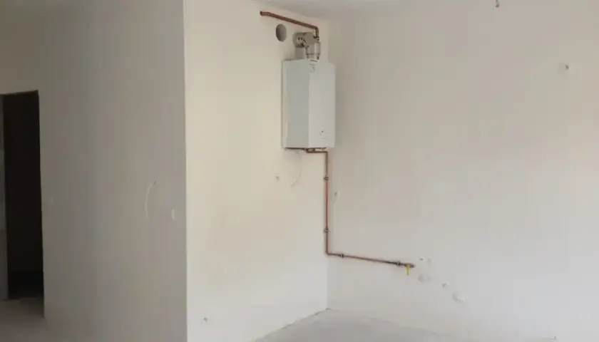 Zabudowa pieca gazowego w rogu pomieszczenia, z miedzianymi rurami doprowadzającymi gaz i wodę.