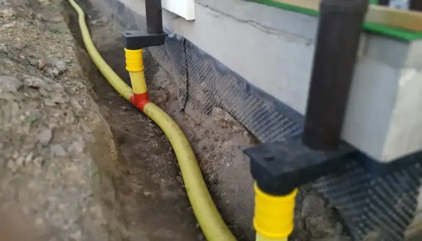 System odprowadzenia wody z rynien w żółtej rurze, biegnącej w wykopie przy fundamencie domu.