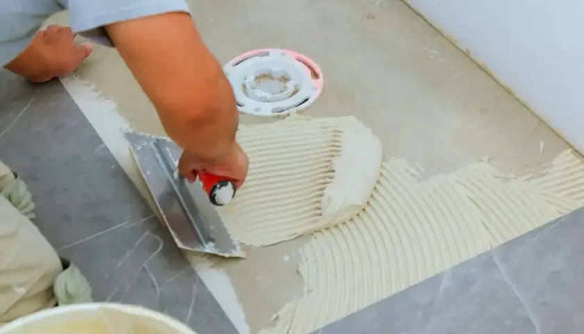 Płytkarz rozprowadza klej kielnią zębatą, przygotowując podłoże pod płytki 60x60.