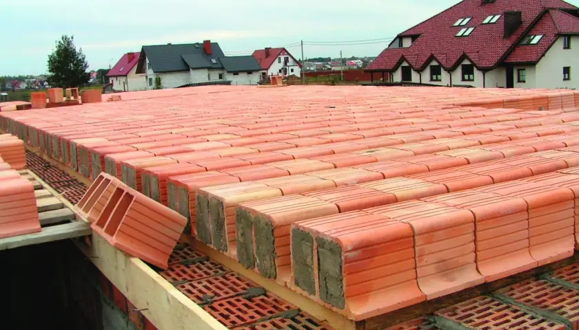 Strop ackermana w budowie, rzędy pustaków ceramicznych czekają na betonowanie. W tle domy z czerwonymi dachami.